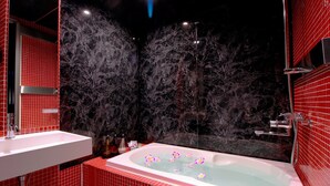 A bathroom with a marble wall, a bathtub with flower petals, and a red-tiled floor.