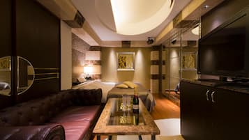 Une chambre d’hôtel moderne avec un canapé, une petite table avec des verres et une bouteille, un lit, une télévision et un mur décoratif.