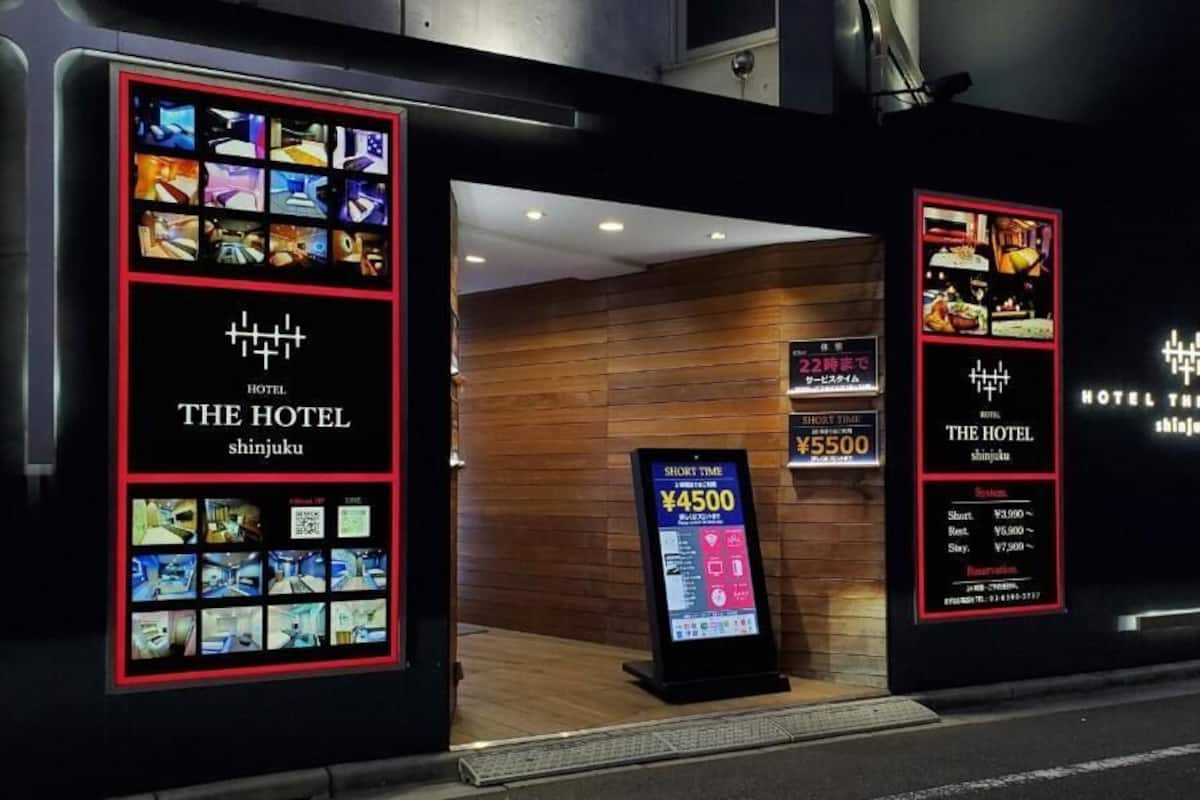 The exterior of a hotel with a modern design, featuring a prominent entrance with illuminated signage displaying room rates and amenities.
