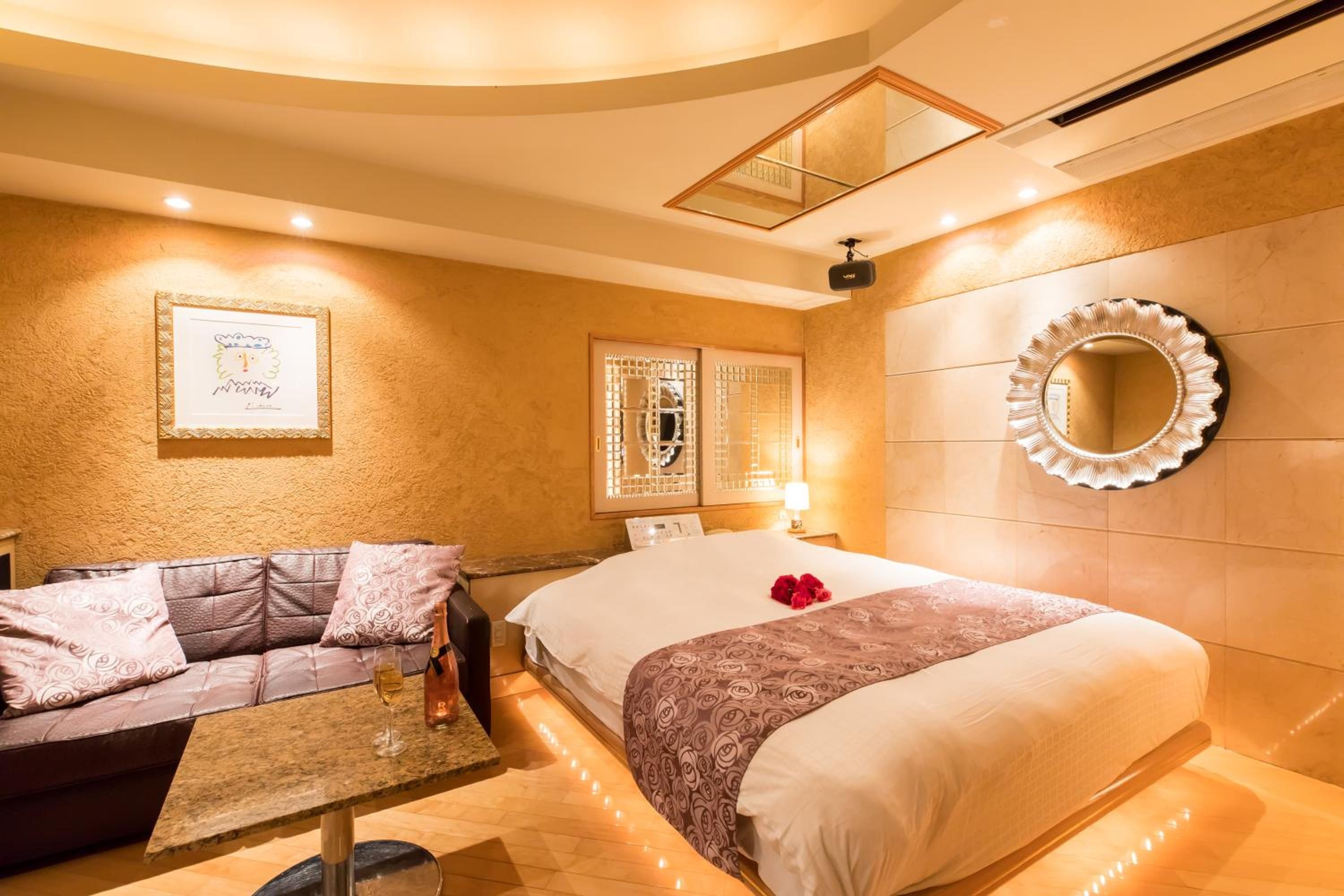 A hotel room with a bed, a sofa, a small table with a glass, and a mirror on the wall.