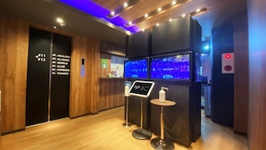 A modern lobby with wooden flooring, a reception desk, and directional signs to various floors.