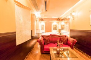Habitación de hotel con un sofá rojo, una mesita de cristal y un minibar.