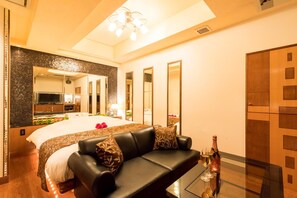 Una habitación de hotel moderna con una cama grande, un sofá de cuero, una mesa de centro de vidrio y un minibar.