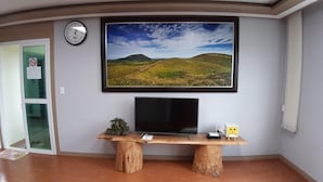 A room with a wooden desk, a flat-screen TV, and a framed landscape painting on the wall. - Woojinsam Pension (Jeju City)
