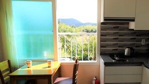 A small kitchen with a view of greenery and mountains through a window. - Woojinsam Pension (Jeju City)