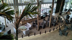 A spacious indoor area with multiple seating arrangements, including sofas and chairs, surrounded by tall palm trees. - UCSI Hotel Kuching (Kuching)