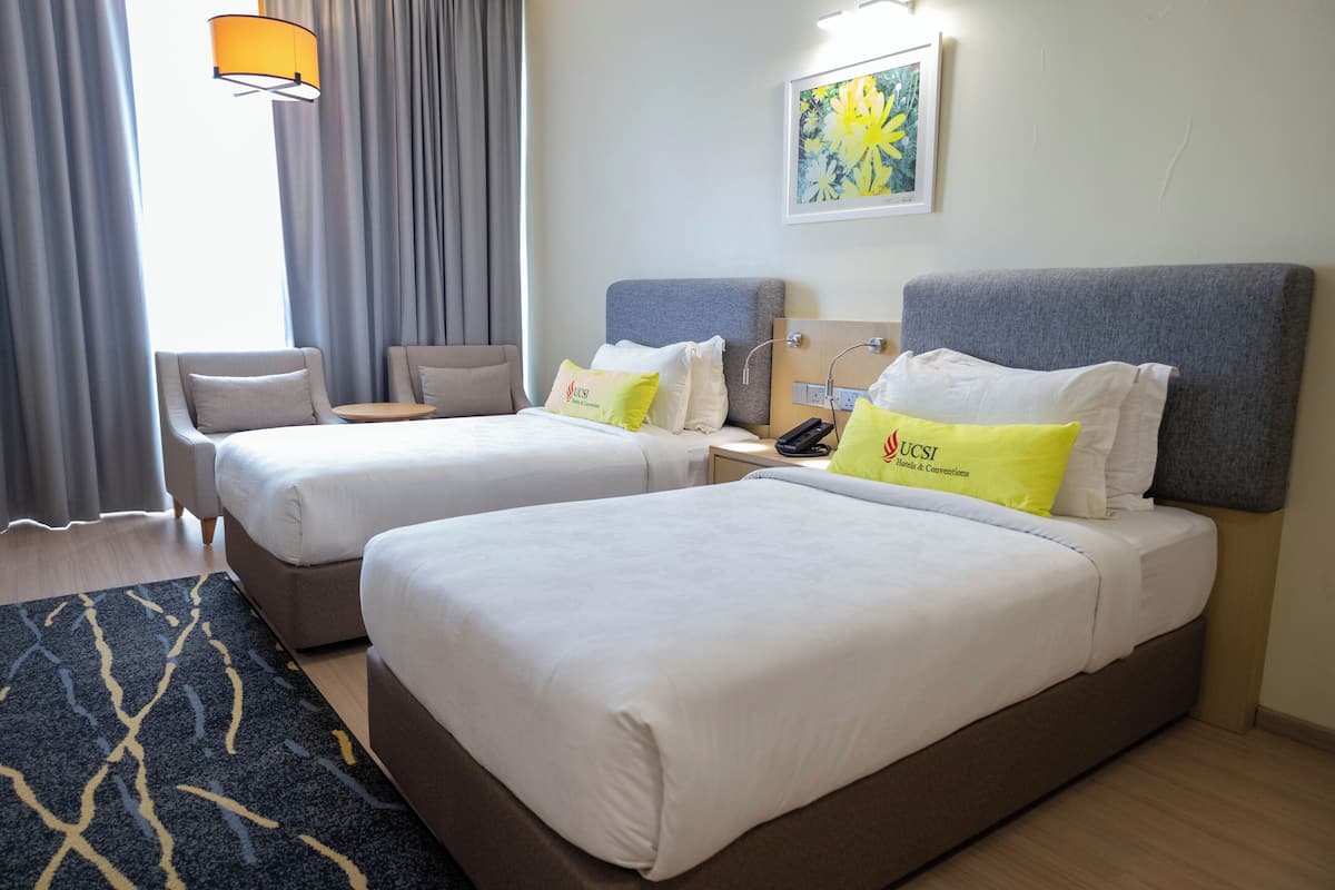 A hotel room with two beds, a small table, a chair, a lamp, and a painting on the wall.