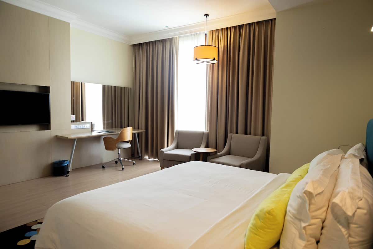 A hotel room with a large bed, a desk with a chair, a television, and a window with curtains.
