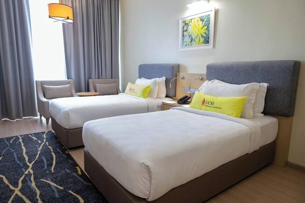 A hotel room with two beds, a desk, a chair, a lamp, and a painting on the wall.