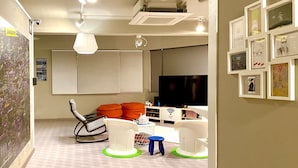 A modern living room with a flat-screen TV, a white sofa, orange cushions, a rocking chair, and a coffee table. - Sohostel Korea (Busan)