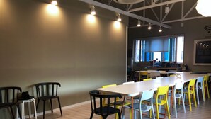 A conference room with a long table and chairs, a kitchenette in the background, and large windows allowing natural light. - Sohostel Korea (Busan)