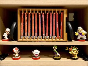 A shelf with a row of red video game cases, a Mario figurine, and several other character figurines. - Sohostel Korea (Busan)