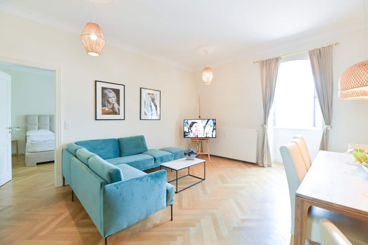 A modern living room with a blue sofa, a TV on a stand, and a dining area with a table and chairs.