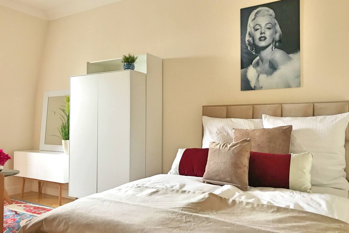 A bedroom with a bed, a dresser, a mirror, and a painting on the wall.