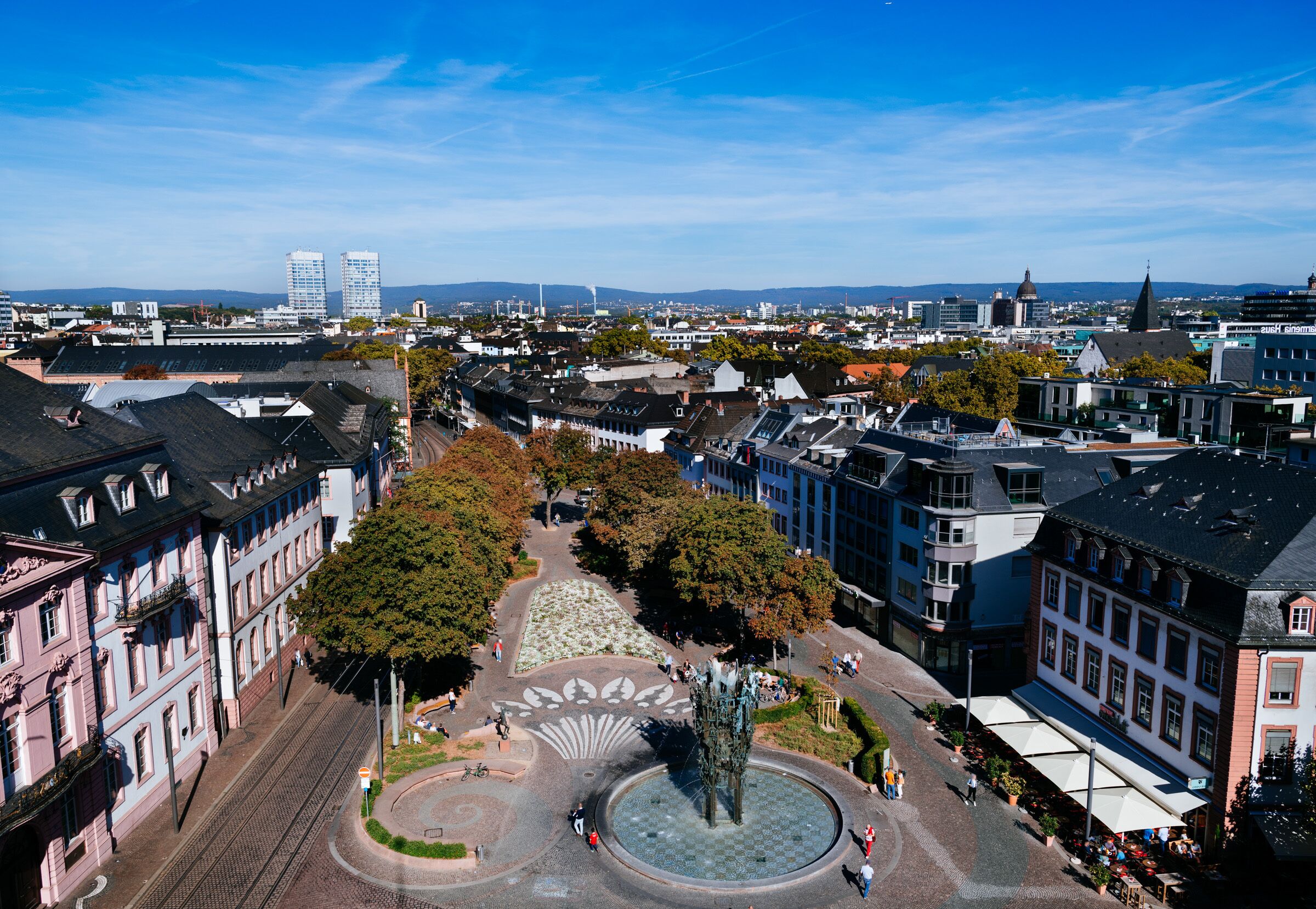 An aerial view of a city square with historic buildings, a central fountain, and tram tracks.