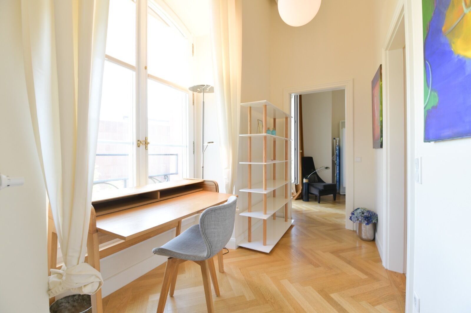 Ein Zimmer mit einem Holztisch, einem Stuhl, einem Bücherregal und einem Fenster mit Vorhängen.
