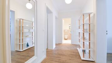 Un pasillo con suelo de madera, paredes blancas y estanterías empotradas con toallas dobladas.