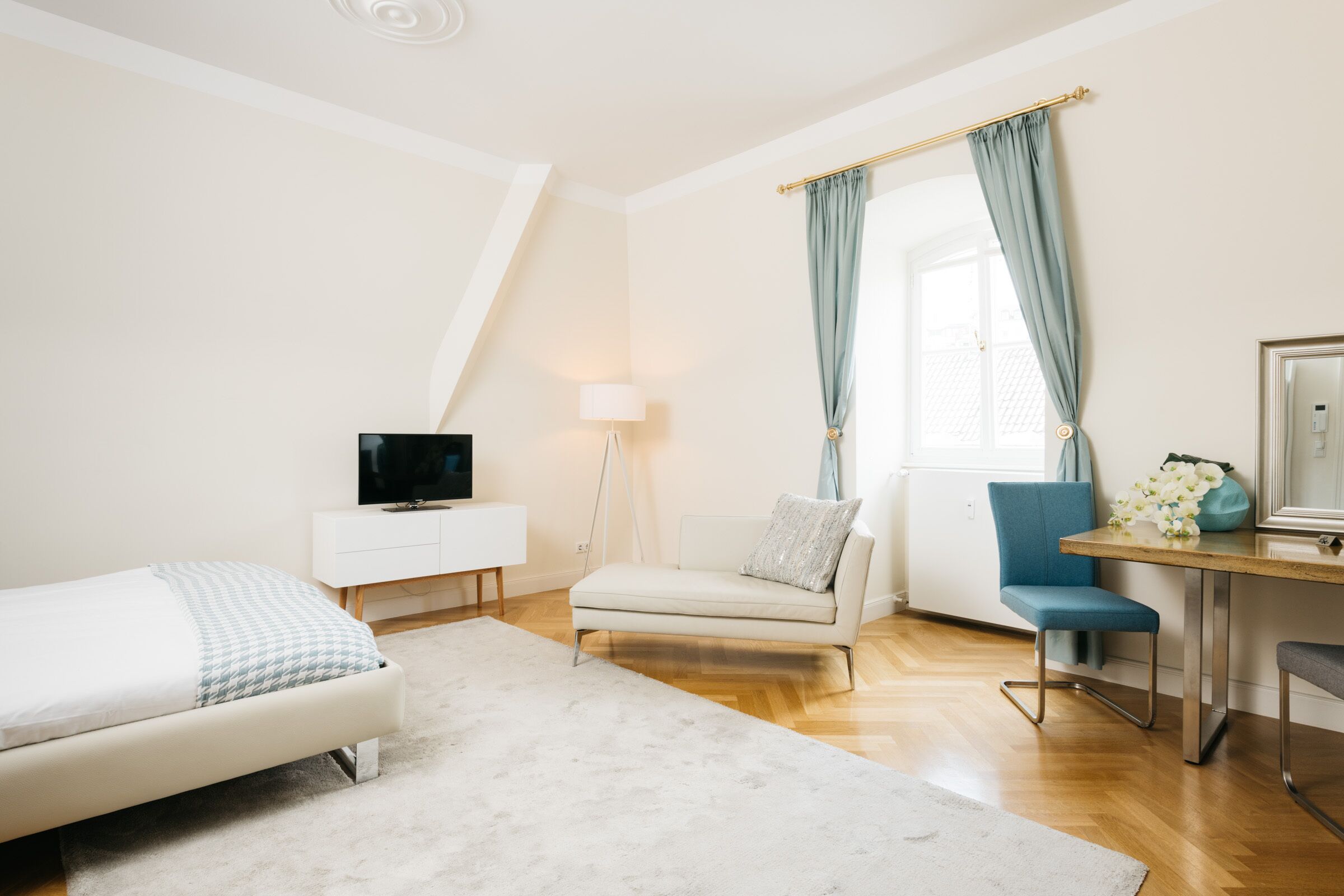 Een moderne slaapkamer met een bed, een bureau, een stoel, een televisie en een raam met gordijnen.