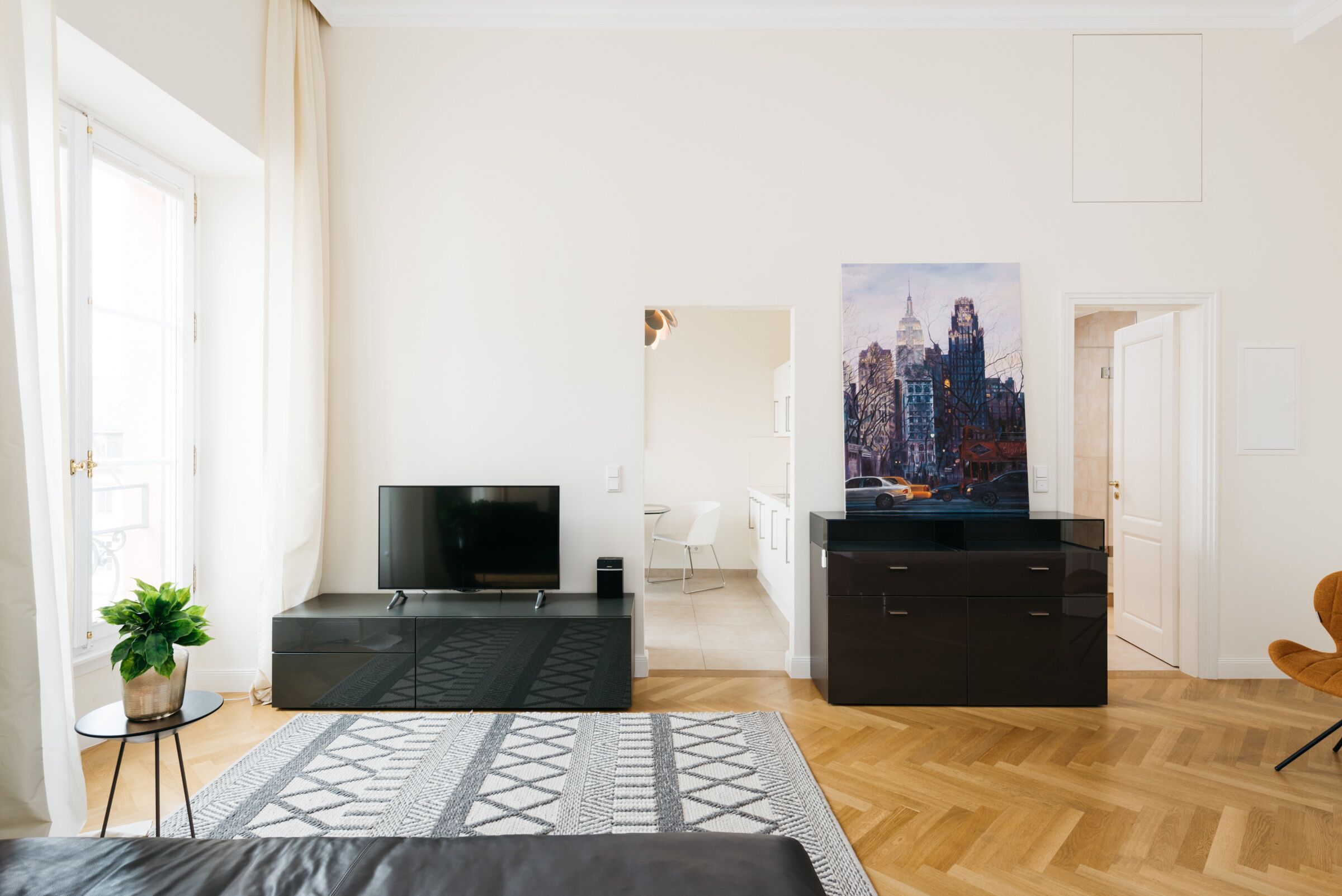 Una sala moderna con un televisor de pantalla plana, un mueble de madera oscura, un tapete estampado y una pintura de un paisaje urbano en la pared.