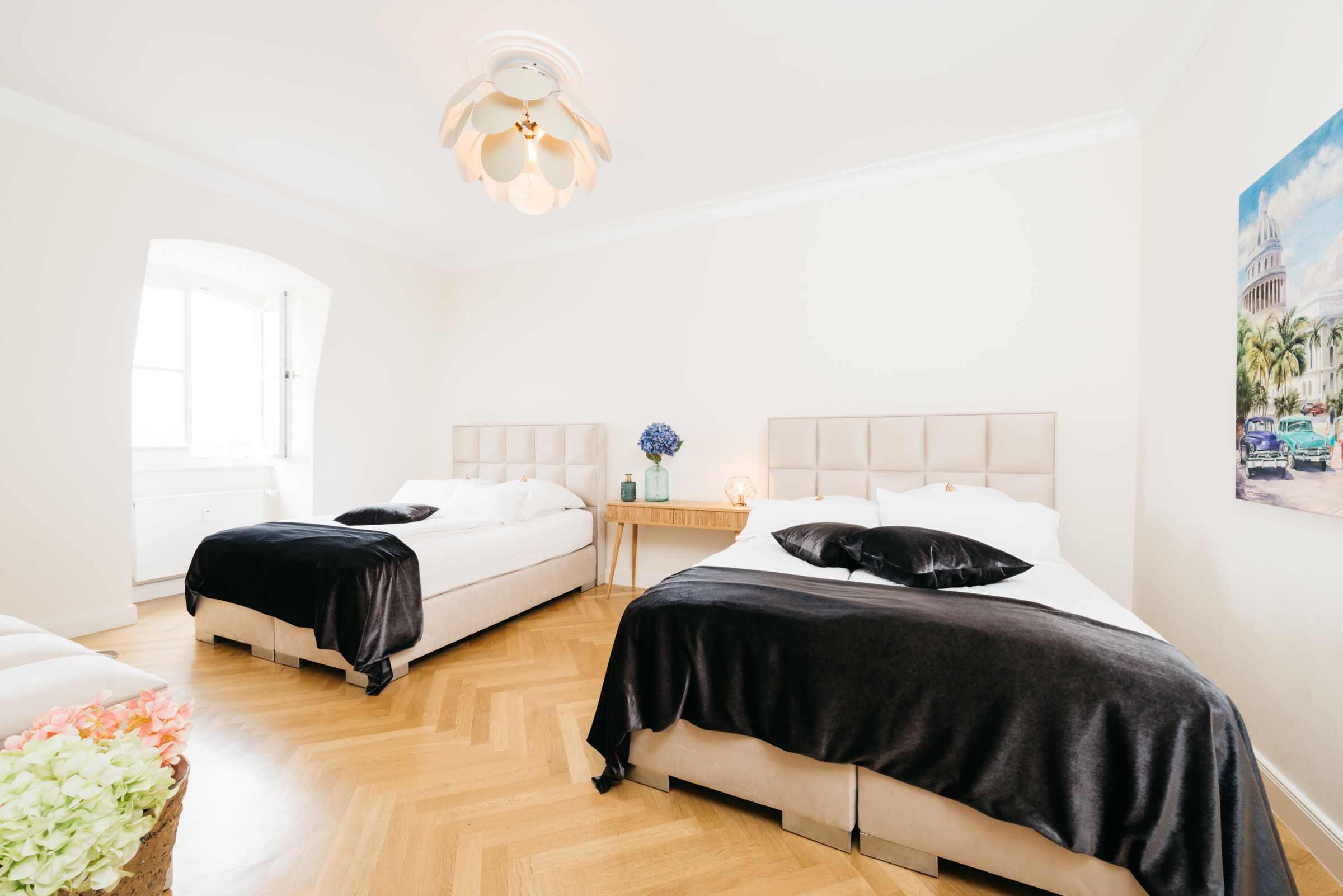 Habitación de hotel con dos camas, piso de madera, una mesita de noche con un florero y un cuadro en la pared.