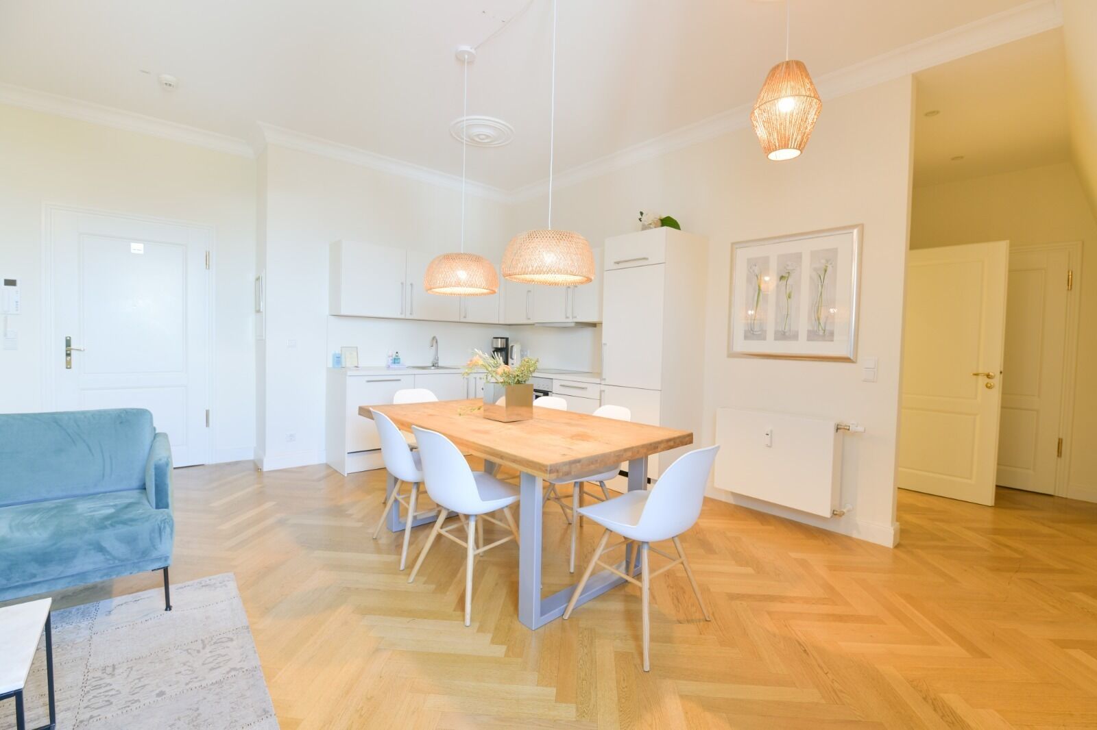 A modern kitchen with white cabinets, a wooden dining table, and pendant lights.