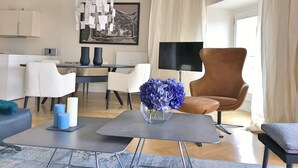 A modern living room with a dining area, a large painting, and a brown leather armchair. - The Apartment Suite Osteiner Hof (Mainz)