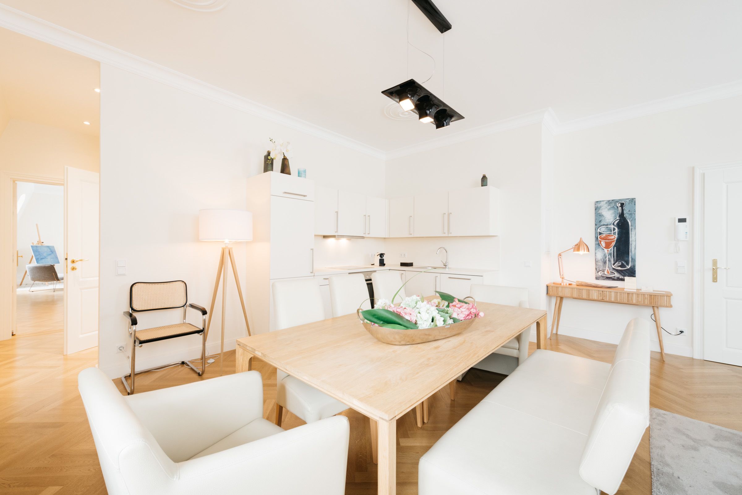 Una cucina moderna con mobili bianchi, un tavolo da pranzo in legno e una ciotola con fiori.