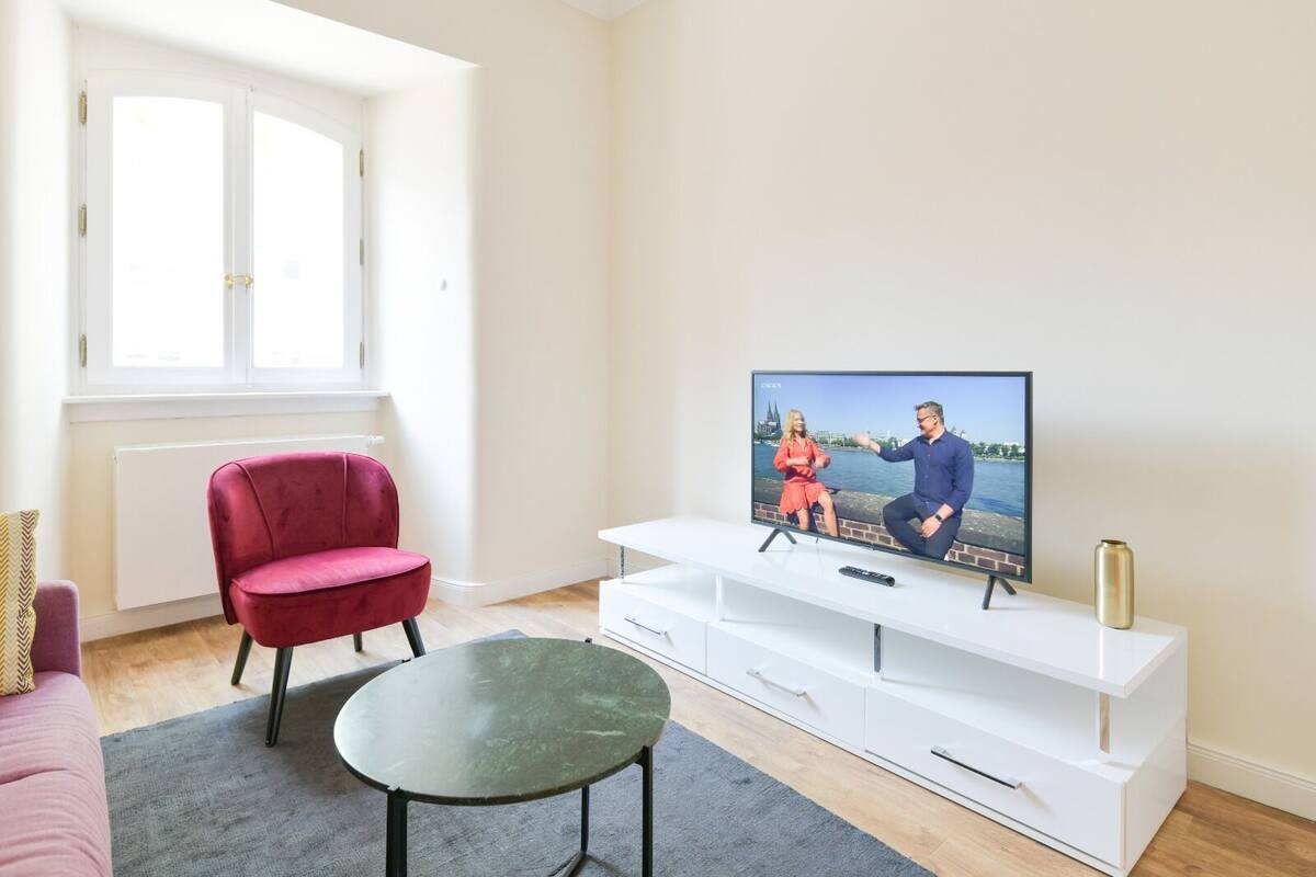 A living room with a television, a red chair, a small table, and a white entertainment unit.