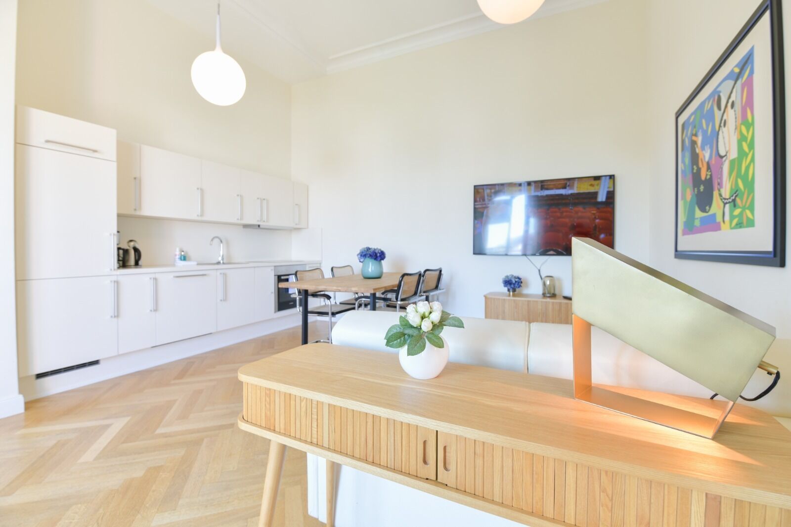 A modern kitchen with white cabinets, a wooden dining table, and a vase with flowers.