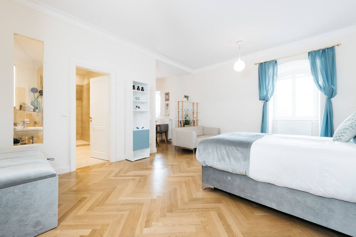 A modern bedroom with a bed, a seating area, and a walk-in closet.