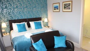 A bedroom with a bed, two pillows, a nightstand, a lamp, a chair, and a wall with a framed picture. - Athol Guest House (Filey)