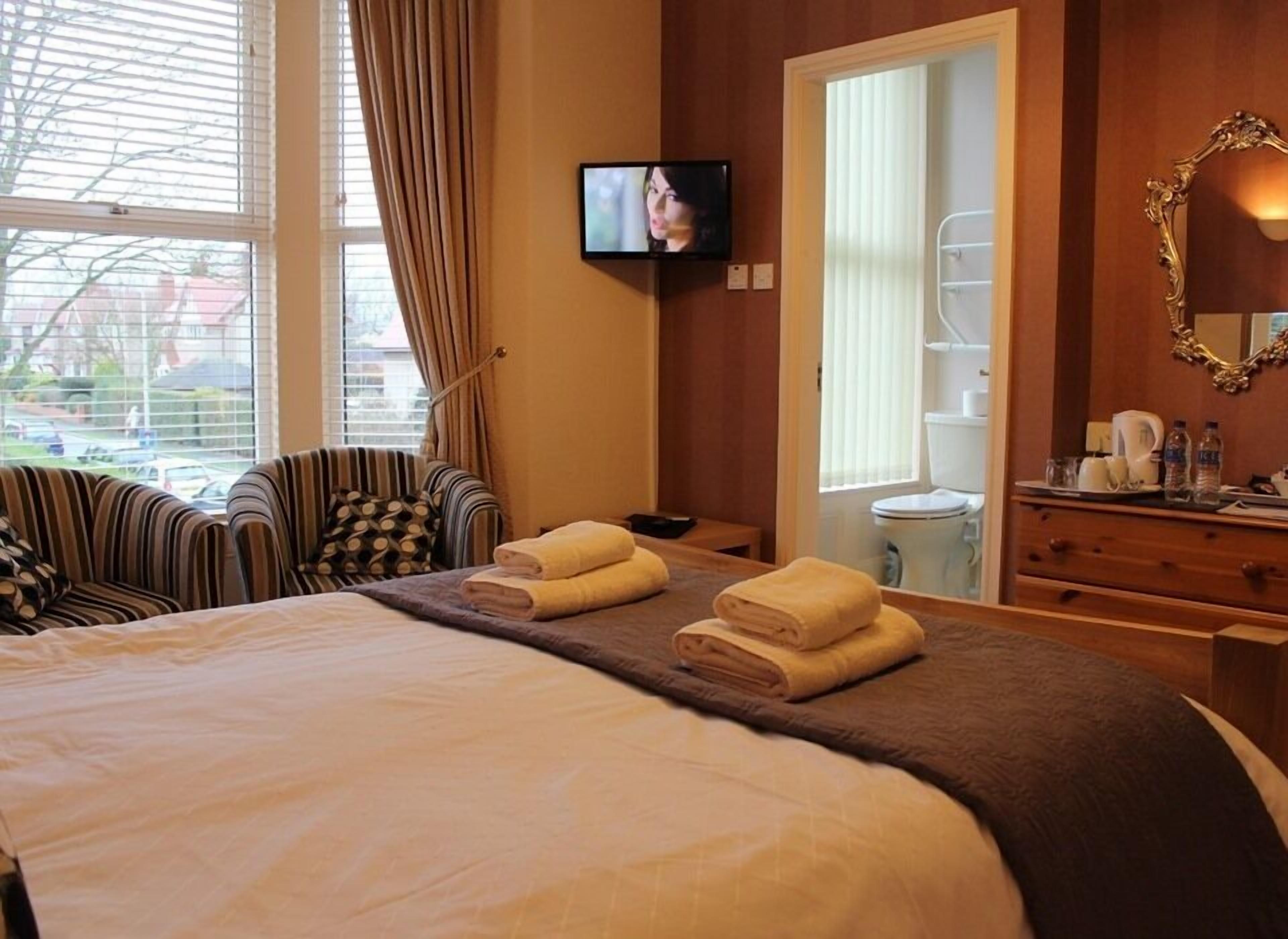 A hotel room with a bed, two armchairs, a television, a bathroom, and a dresser with toiletries.