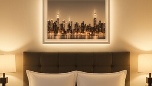 Quarto de hotel com uma cama grande, duas luminárias de cabeceira e um quadro com uma vista urbana na parede.