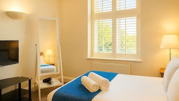A hotel room with a bed, a TV, a mirror, a window with blinds, and a lamp.