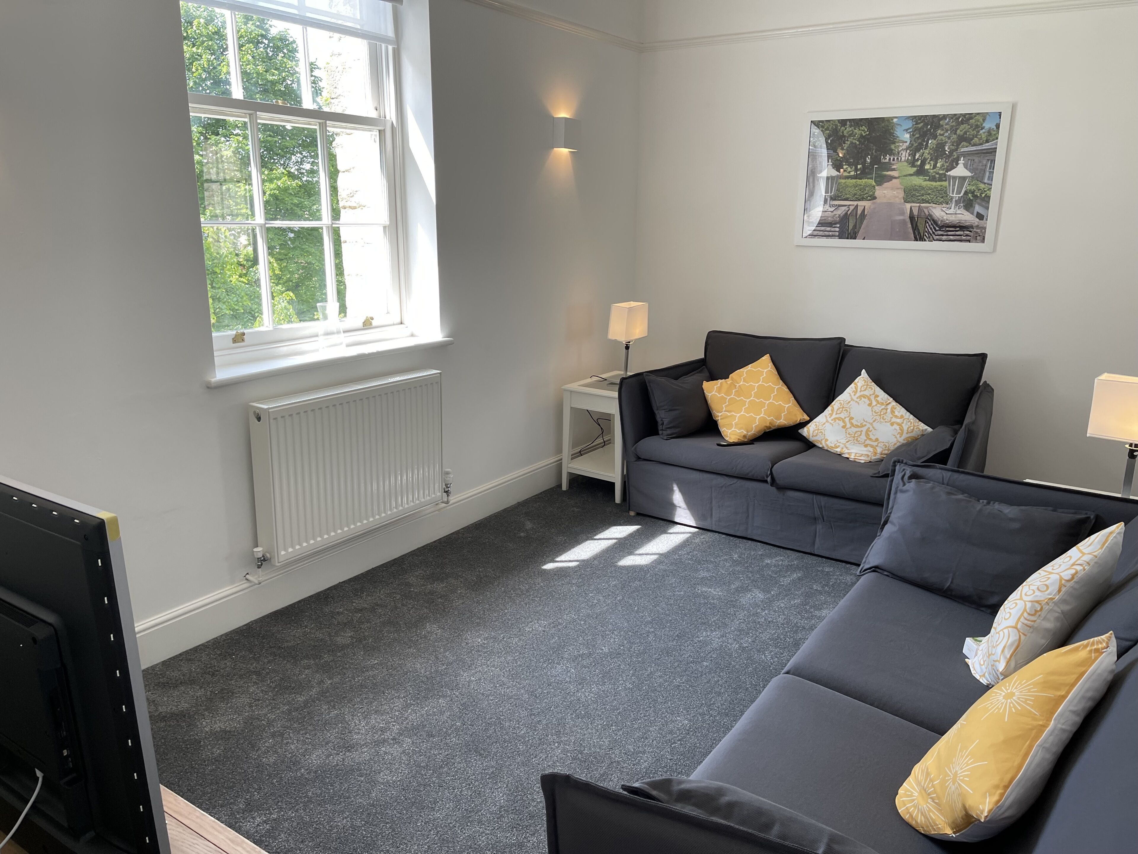A modern living room with a grey sofa set, a white side table, and a framed picture on the wall.