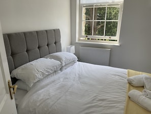 Relax in a cozy space with a large bed, tufted headboard, and serene views of the outdoors.