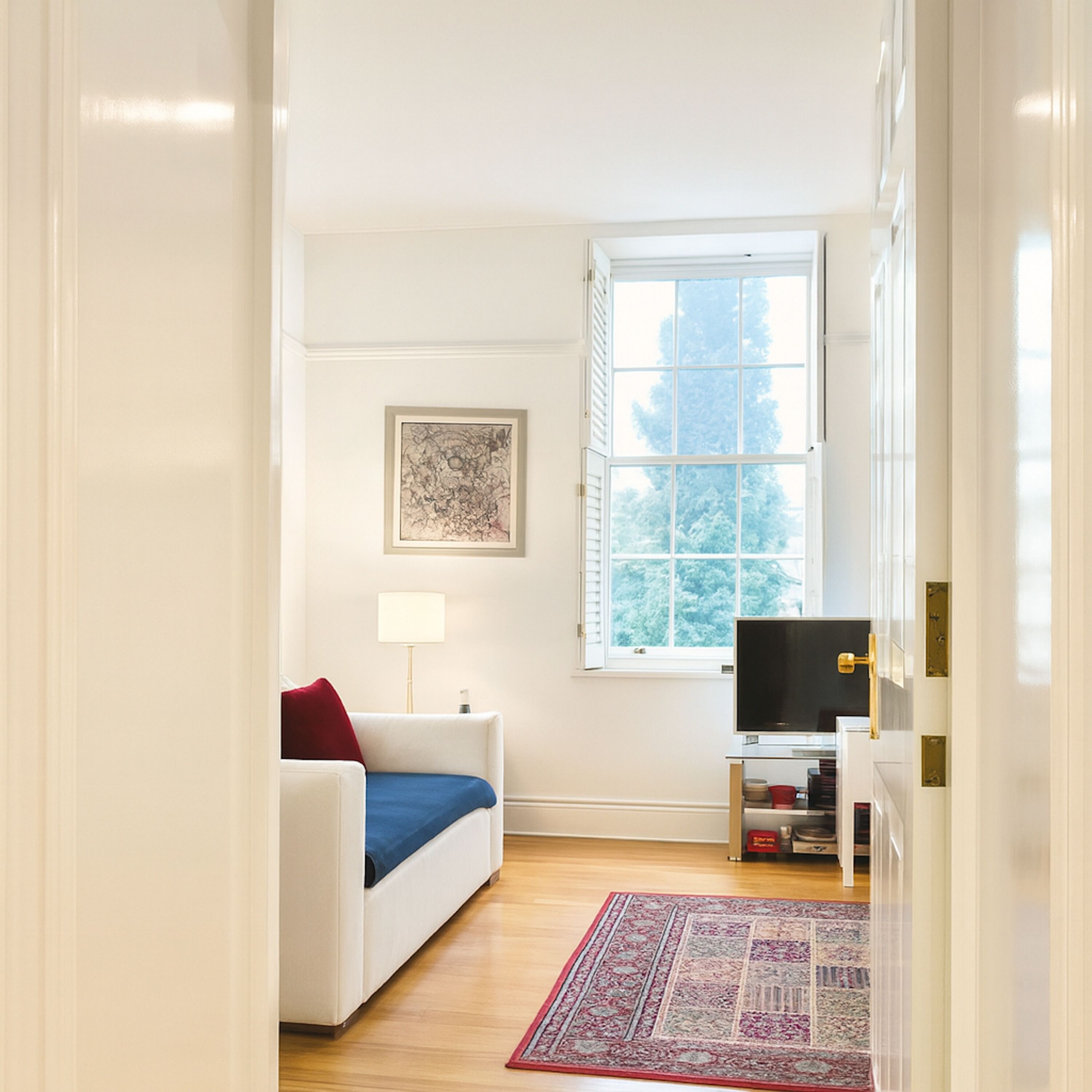 A compact living space with a sofa, a television, a window with shutters, and a rug.
