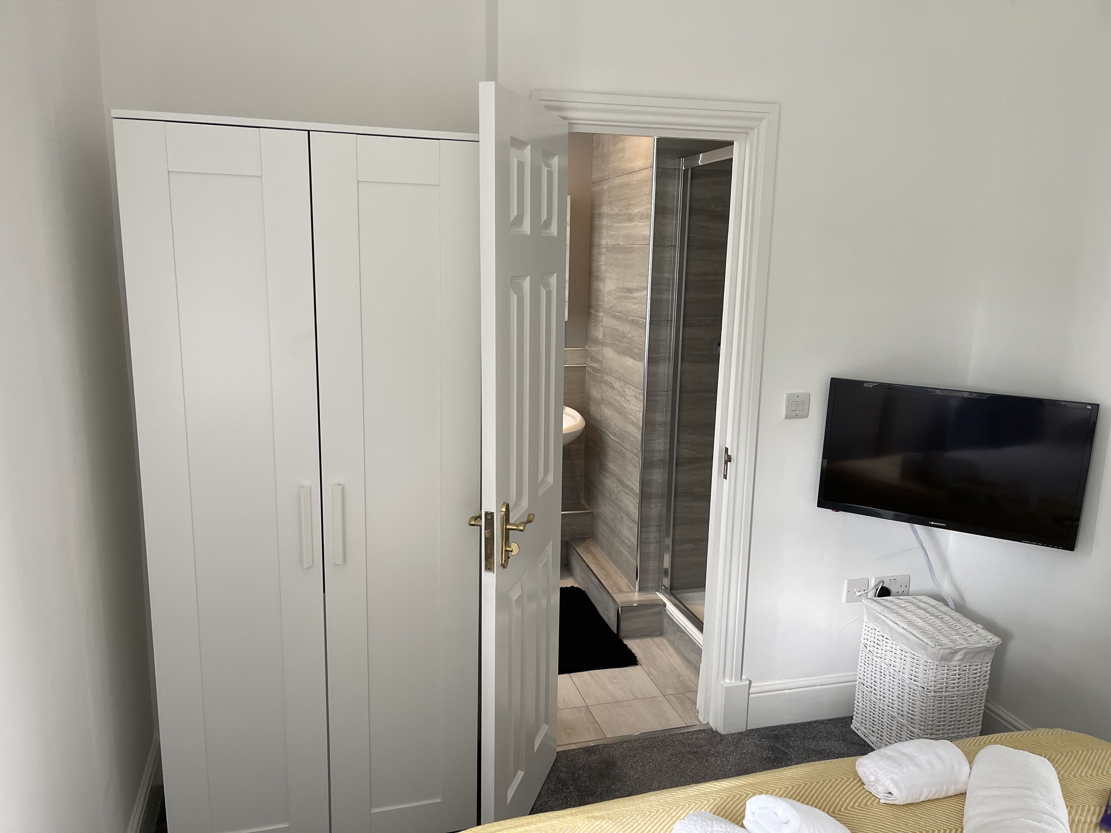 A hotel room with a bed, a TV mounted on the wall, a white wardrobe, and a shower area.