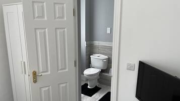 Un baño con inodoro, lavamanos y un televisor negro montado en la pared.