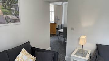 En moderne stue med en sort sofa, et lille hvidt sofabord med en lampe, samt et spiseområde med bord og stole.