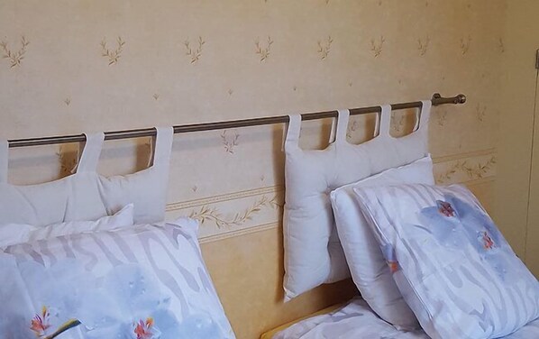 Una cama con cabecera metálica y almohadas blancas, frente a una pared con estampado floral.