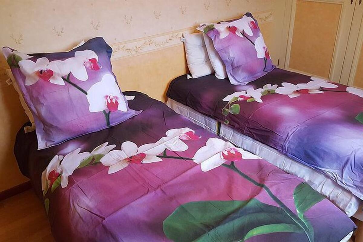 Two beds with floral bedding in a room with a wooden floor and a beige wall.