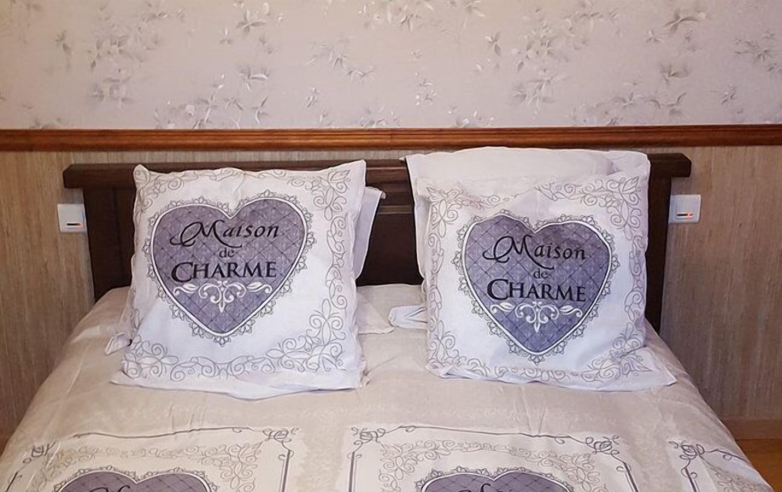 Un lit agrémenté de deux coussins décoratifs sur lesquels figure l’inscription « Maison de Charme ».