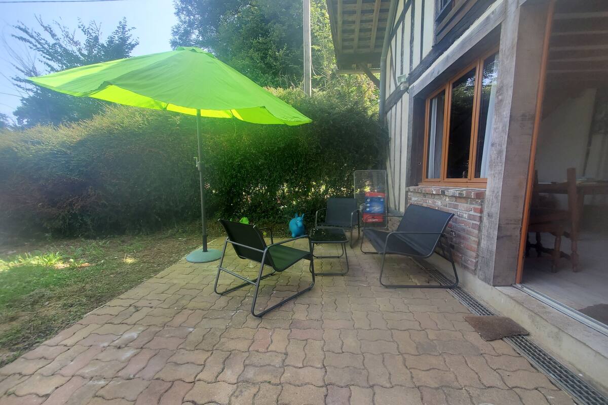 A patio with a green umbrella, two chairs, and a table.