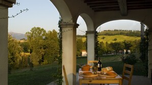 Ein überdachter Essbereich im Freien mit Tisch für zwei Personen, mit Blick auf einen Weinberg und sanfte Hügel.