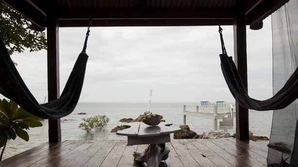Una terraza de madera con una mesa y sillas, con vista a una costa rocosa y un muelle.
