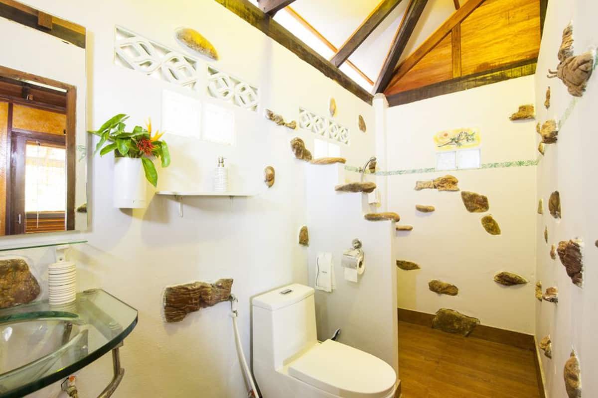 Ein Badezimmer mit Waschbecken aus Glas, einer weißen Toilette und dekorativen Steinen an den Wänden.