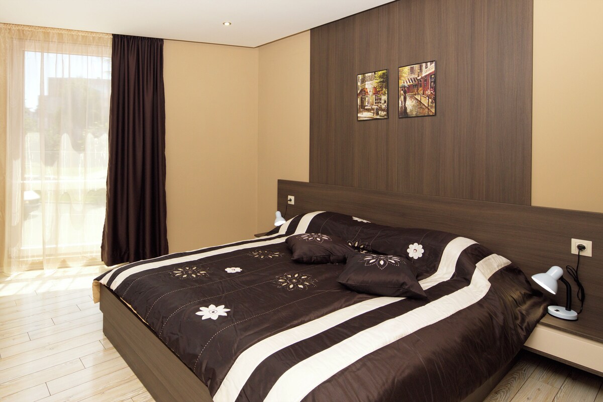 Un dormitorio con una cama grande, una mesita de noche, una lámpara y dos cuadros colgados en la pared.