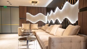 Um lobby moderno com sofá de canto, mesas redondas e um design de parede diferenciado.