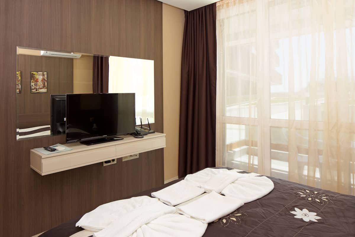 Ein Hotelzimmer mit Bett, Fernseher, Spiegel und einem Fenster mit Vorhängen.